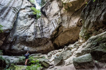 Gautschgrotte Eine Person steht in einer felsigen Schlucht, umgeben von hohen, steilen Wänden und grüner Vegetation, die eine ruhige, natürliche Atmosphäre schafft.