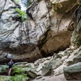 Gautschgrotte Eine Person steht in einer felsigen Schlucht, umgeben von hohen, steilen Wänden und grüner Vegetation, die eine ruhige, natürliche Atmosphäre schafft.