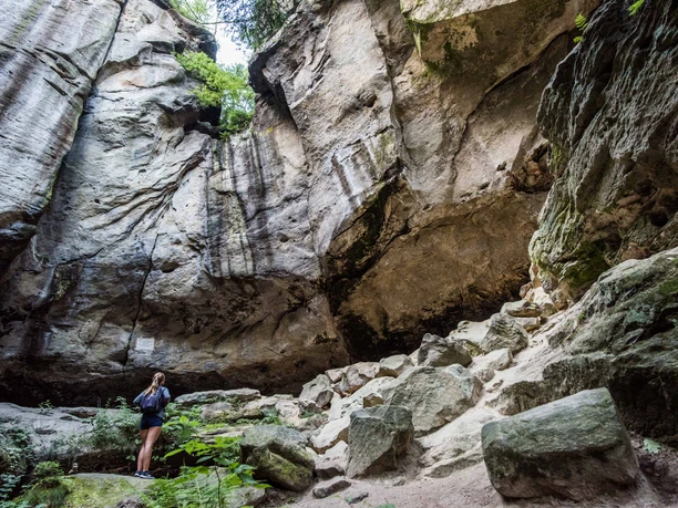 Gautschgrotte Eine Person steht in einer felsigen Schlucht, umgeben von hohen, steilen Wänden und grüner Vegetation, die eine ruhige, natürliche Atmosphäre schafft.