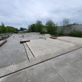 Jugendfreizeitpark Wermelskirchen Moderner Skatepark mit glatten Betonflächen, Rails und Rampen, umgeben von grünen Bäumen und Büschen.