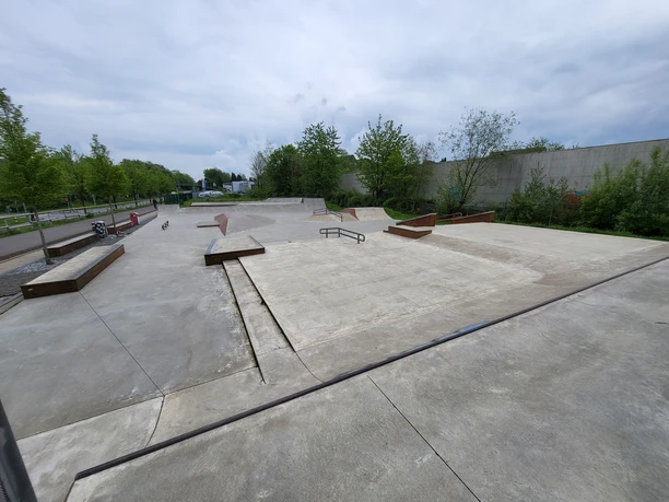 Jugendfreizeitpark Wermelskirchen Moderner Skatepark mit glatten Betonflächen, Rails und Rampen, umgeben von grünen Bäumen und Büschen.