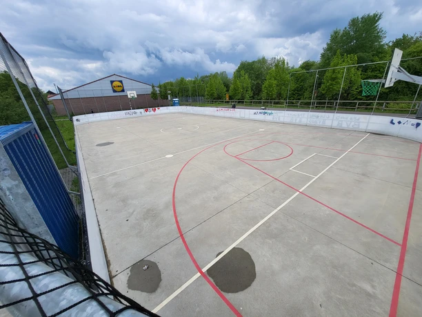 Jugendfreizeitpark Wermelskirchen Ein leerer, eingezäunter Sportplatz mit Basketballkörben, umgeben von Bäumen und einem Supermarkt.
