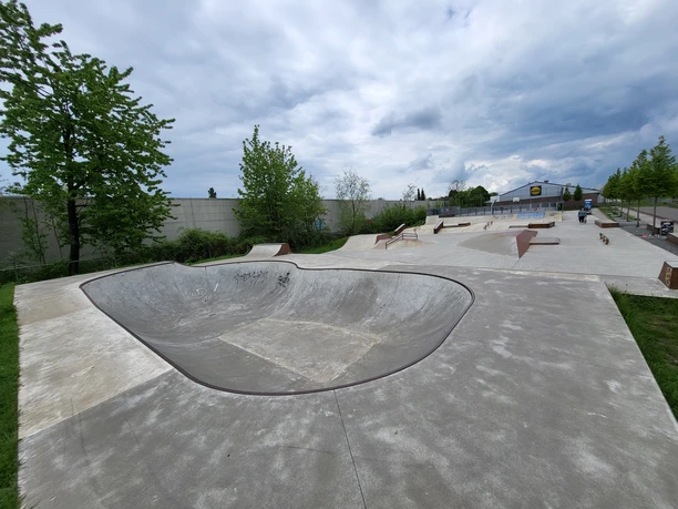Jugendfreizeitpark Wermelskirchen Weitläufiger Skatepark mit Halfpipe und mehreren Rampen, umgeben von Bäumen unter bewölktem Himmel.