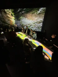 Personen betrachten bei gedämpftem Licht eine große, leuchtende interaktive Karte in einem Ausstellungsraum.