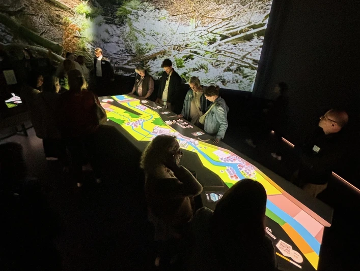Personen betrachten bei gedämpftem Licht eine große, leuchtende interaktive Karte in einem Ausstellungsraum.