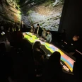 KEW3.jpg Personen betrachten bei gedämpftem Licht eine große, leuchtende interaktive Karte in einem Ausstellungsraum.