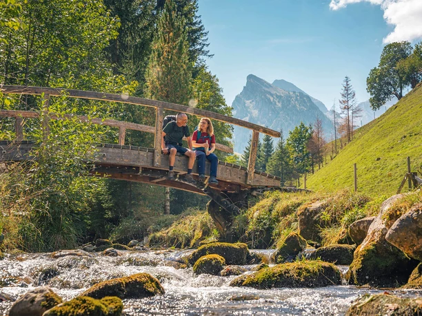 Durch den Naturpark Diemtigtal wandern Wanderer ruhen sich auf einer Holzbrücke aus und lassen die Beine baumeln