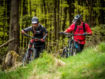 2 Mountainbiker schieben ihre Bikes über eine Lichtung 2 Mountainbiker schieben ihre Bikes über eine Lichtung