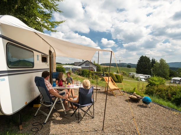 Campingpark im Bergischen Land <p>Familie entspannt vor Wohnwagen auf sonnigem Campingplatz im Grünen, mit Weitblick über Hügel.</p>