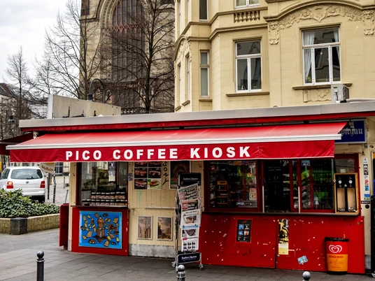 Pico Coffee Das Bild zeigt den majestätischen Turm der Agneskirche in Köln, hinter dem Kiosk Café im Agnesviertel.The picture shows the majestic tower of the Agneskirche in Cologne, behind the Kiosk Café in the Agnesviertel.