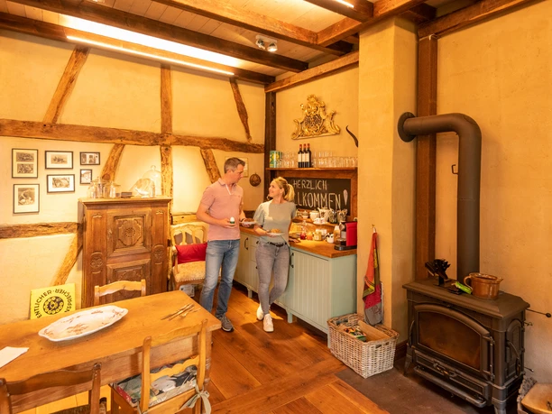 Ferienwohnung Hof Tüschenbonnen Zwei Personen in rustikalem Raum mit Holzofen, antiken Möbeln und herzlicher Atmosphäre.