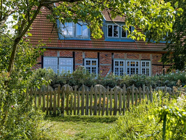 Ein Weg führt durch einen Garten zu einem Haus. Vor dem Haus steht ein Zaun.