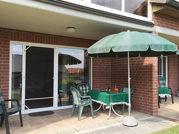 Terrasse Sonnige Terrasse am Backsteinhaus mit gedecktem Tisch, Stühlen und grünem Sonnenschirm.