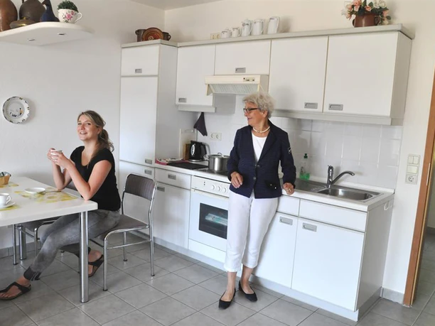 hochwertige, offene Küche mit Essplatz Zwei lächelnde Frauen in einer offenen, weißen Küche mit Esstisch und Küchenzeile.