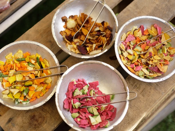 "Jrön un Jedön" Vier Schalen mit bunten, getrockneten Gemüsescheiben auf einem Holztisch, arrangiert für Verkostung.
