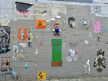 Wall of fame Eine bunte Wand mit kunstvollen Graffitis und Stickern, darunter ein Mario-Spielcharakter und verschiedene Pop-Art-Motive, erweckt urbane Kreativität zum Leben.A colorful wall adorned with artistic graffiti and stickers, including a Mario video game character and various pop-art motifs, bringing urban creativity to life.