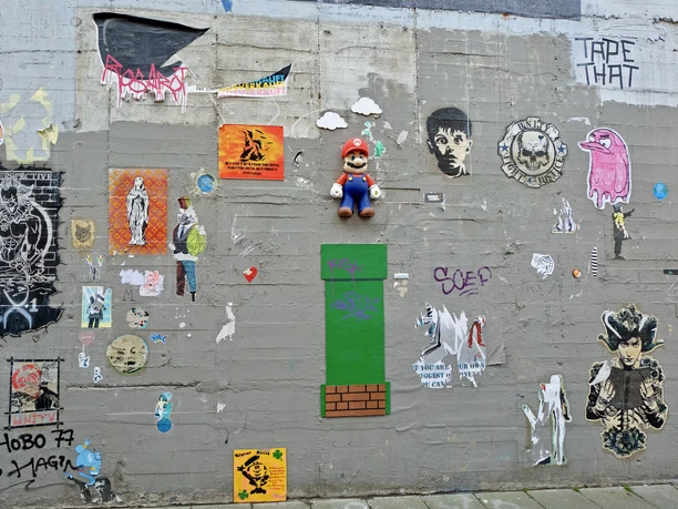 Wall of fame Eine bunte Wand mit kunstvollen Graffitis und Stickern, darunter ein Mario-Spielcharakter und verschiedene Pop-Art-Motive, erweckt urbane Kreativität zum Leben.