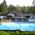 Das Freibad 2004.JPG Öffentliches Freibad mit Schwimmern, umgeben von Bäumen und Gebäuden unter einem klaren Himmel.