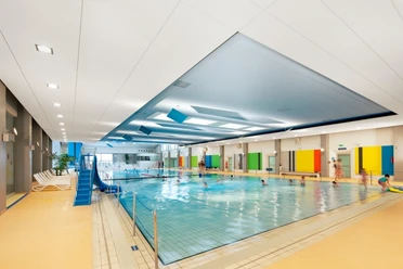Hallenbad Bad Nenndorf Ein modernes Hallenbad mit großen Fenstern, farbenfrohen Wänden und einem Becken voller Schwimmer.