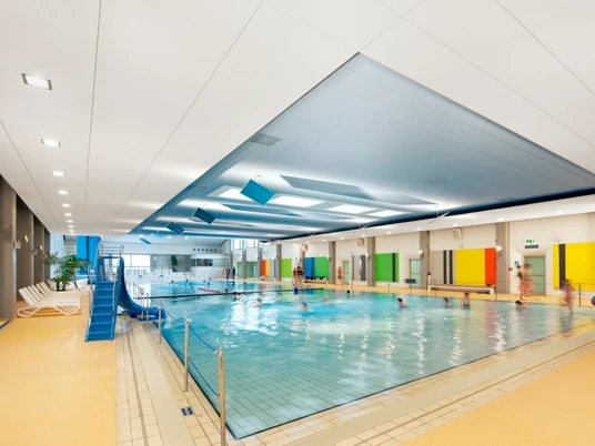 Hallenbad Bad Nenndorf Ein modernes Hallenbad mit großen Fenstern, farbenfrohen Wänden und einem Becken voller Schwimmer.