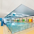 Hallenbad BN.jpg Ein modernes Hallenbad mit großen Fenstern, farbenfrohen Wänden und einem Becken voller Schwimmer.