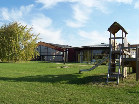 Hallenbad Bad Nenndorf Außenbereich Ein modernes Hallenbad mit Glasfassade, umgeben von einer großzügigen Rasenfläche und einem Spielplatz.