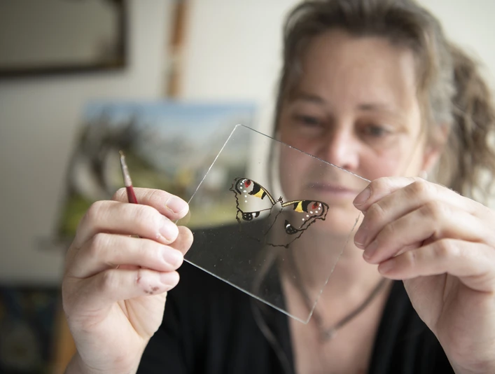 Hinterglasmalerei Dichtl Künstlerin hält eine Glasplatte mit Schmetterlingsbild in der Hand.