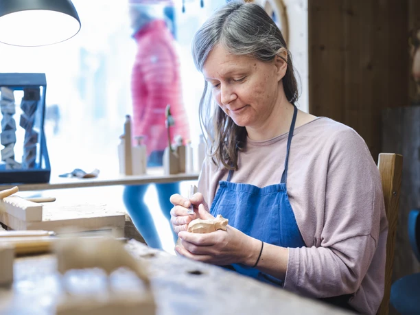 Holzschnitzkunst Jochner Eine Frau schnitzt in ihrer Werkstatt ein kleines Holzobjekt.