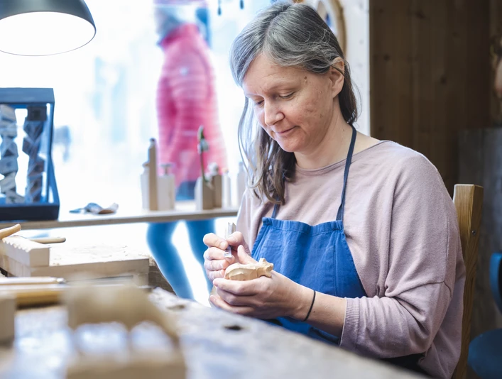 Holzschnitzkunst Jochner Eine Frau schnitzt in ihrer Werkstatt ein kleines Holzobjekt.