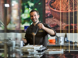 Chocolatier Linus Kässer Ein Chocolatier in Arbeitskleidung gießt Schokolade in Formen.
