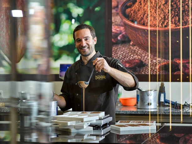 Chocolatier Linus Kässer Ein Chocolatier in Arbeitskleidung gießt Schokolade in Formen.
