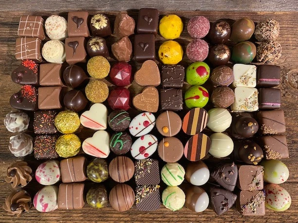 Chocolaterie Amelie Linus Kässer Verschiedene Pralinen in bunten Farben und Formen auf hölzernem Untergrund.