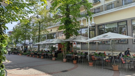 Ristorante Pizzeria Piazza.jpg Auf dem Bild ist die einladende Außenansicht des Restaurants zu sehen, umgeben von üppigen, grünen Bäumen. Gemütliche Sitzgelegenheiten laden dazu ein, die frische Luft zu genießen und im Freien zu speisen.