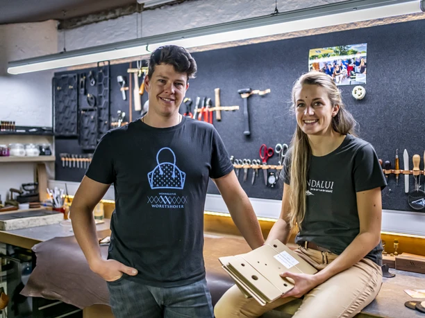 Florian Wöretshofer Lederverarbeitung Andalui Zwei Personen stehen in einer Werkstatt für Lederverarbeitung, umgeben von Werkzeugen.