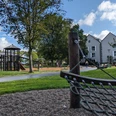 Spielplatz im Kurpark Grünanlage mit Spielplatz, Kletternetz im Vordergrund, Mehrfamilienhäuser und Erwachsene im Hintergrund.