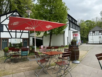 Gemütlicher Außenbereich eines Landgasthofs mit Fachwerk-Fassade, rot-weißem Sonnenschirm und Holzmöbeln.