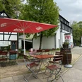 Café Alte Dombach - Außenansicht Gemütlicher Außenbereich eines Landgasthofs mit Fachwerk-Fassade, rot-weißem Sonnenschirm und Holzmöbeln.