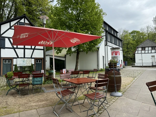 Café Alte Dombach - Außenansicht Gemütlicher Außenbereich eines Landgasthofs mit Fachwerk-Fassade, rot-weißem Sonnenschirm und Holzmöbeln.