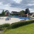 Ein Freibad mit großem Schwimmbecken, roter Rutsche, Sprungturm und Schachspiel auf der Terrasse.