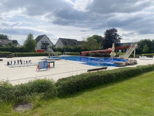 Erlebnisfreibad Beverungen Ein Freibad mit großem Schwimmbecken, roter Rutsche, Sprungturm und Schachspiel auf der Terrasse.