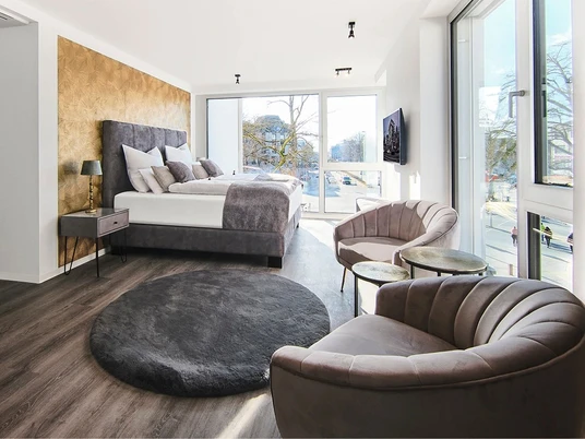 Hotel Kump 365, Zimmer Modernes Hotelzimmer mit großem Bett, goldener Wand, samtigen Sesseln und einem flauschigen Teppich.