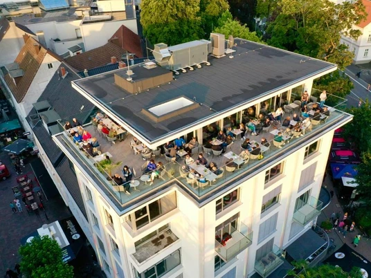 Dachterrasse eines modernen Hotels mit Gästen, die bei Sonnenuntergang den Ausblick genießen.