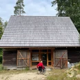 Blockscheune Waldhusche Eine Person im Rollstuhl trägt eine rote Jacke und nähert sich einem hölzernen Gebäude mit großen Doppeltüren, umgeben von Bäumen.A person in a wheelchair wears a red jacket and approaches a wooden building with large double doors, surrounded by trees.Osoba na vozíku má na sobě červenou bundu a přijíždí k dřevěné budově s velkými dvojitými dveřmi, obklopené stromy.Osoba na wózku inwalidzkim ma na sobie czerwoną kurtkę i zbliża się do drewnianego budynku z dużymi podwójnymi drzwiami, otoczonego drzewami.Een persoon in een rolstoel draagt een rode jas en nadert een houten gebouw met grote dubbele deuren, omringd door bomen.Una persona in sedia a rotelle indossa una giacca rossa e si avvicina a un edificio di legno con grandi porte doppie, circondato da alberi.
