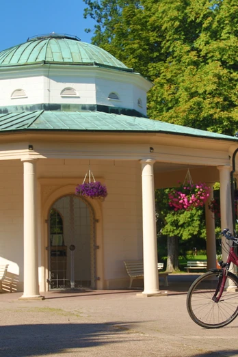 Ein Radfahrer mit Helm studiert eine Karte vor einem historischen Tempel mit Säulen und Blumenampeln.