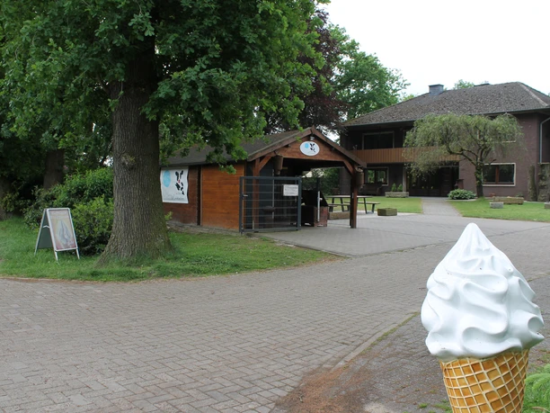 Laxtener Milchbüdchen in Lingen (Ems) ©Emsland Tourismus GmbH (1).JPG Kleines Holzverkaufshäuschen mit Eisskulptur im Vordergrund, umgeben von Bäumen und Hofgebäuden.