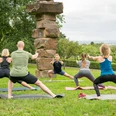 Yoga im Park Menschen machen Yoga im Freien auf einer Wiese nahe einem mehrschichtigen Steinturm.