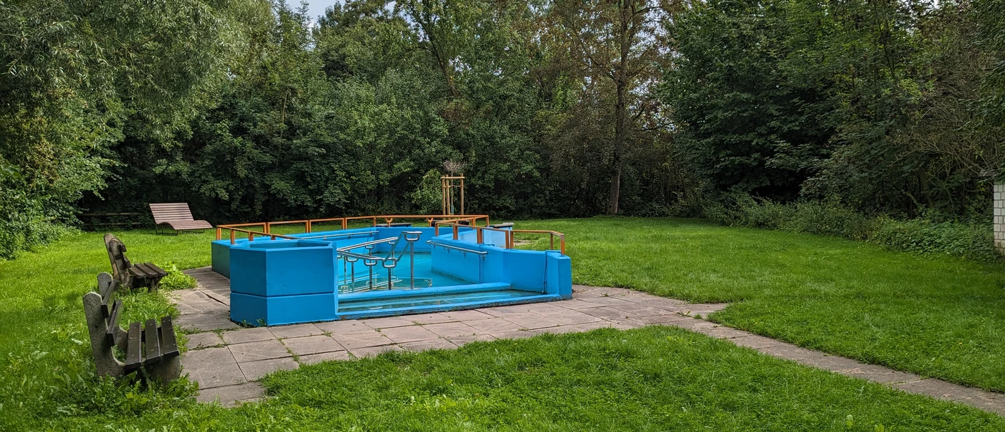 Tretbecken in Amelunxen Blaues Kneipptretbecken, umgeben von Pflastersteinen und Rasen, linksseitig zwei Holzbänke, im Hintergrund Bäume und eine Ruhebank