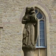Statue an der Kirche Maria-Statue vor einer Kirche aus Sandstein, sie hält ein Kind auf dem Arm. Im Hintergrund Kirchenwand.