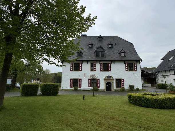 Außenansicht Ein zweigeschossiges, historisches Gebäude mit weißer Fassade und roten Fensterläden.