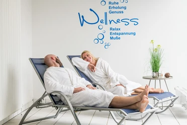 Das Bergische-2020-100-Gesundheit.jpg Entspannte Menschen in Bademänteln liegen auf Wellnessliegen im Spa-Bereich und lächeln einander an.